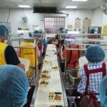 新業(yè)同仁與志工們繫上圍裙、套上防塵帽，戴上口罩，手捧一份份飯包各司其職，為的是準(zhǔn)時(shí)將熱騰騰的飯包送到長(zhǎng)輩手中。