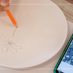 筆尖在素色瓷胚上，輕輕滑過(guò)，對(duì)照著手機(jī)上的圖樣，描繪形塑出個(gè)人獨(dú)特的風(fēng)格。